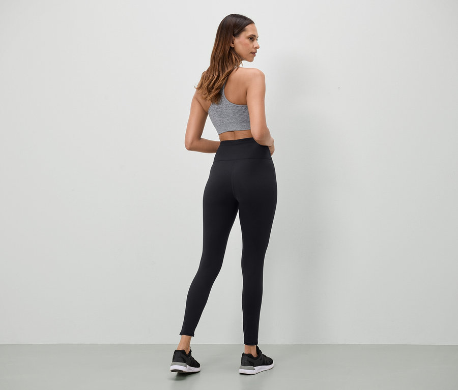 Szürke sportmelltartót és fekete leggingset viselő nő áll háttal a kamerának.