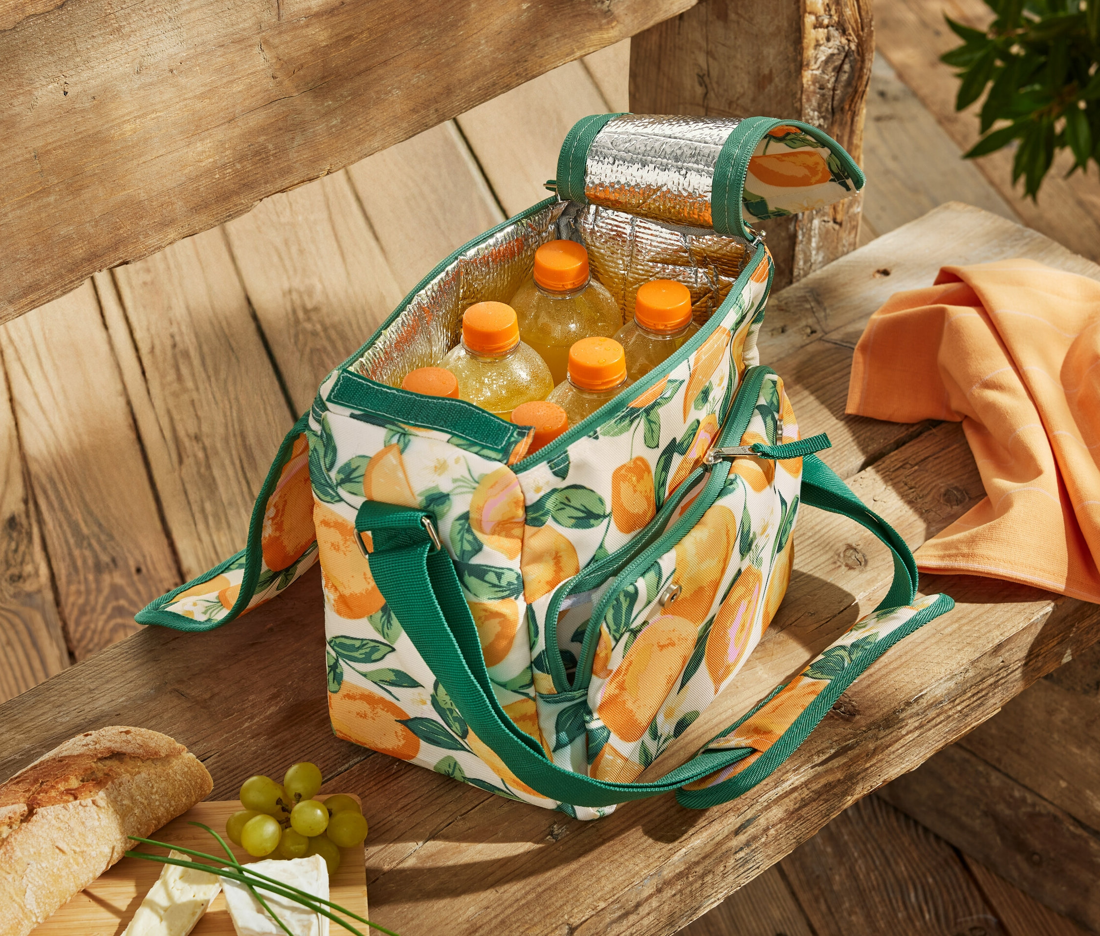 Egy nyitott, citrusmintás mini hűtőtáska tele palackokkal egy fa padon.