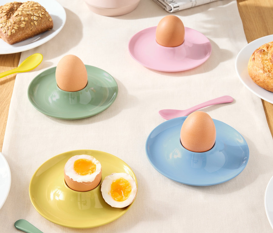 Különböző színű tojástartók tojásokkal és kanállal egy terítőn.
