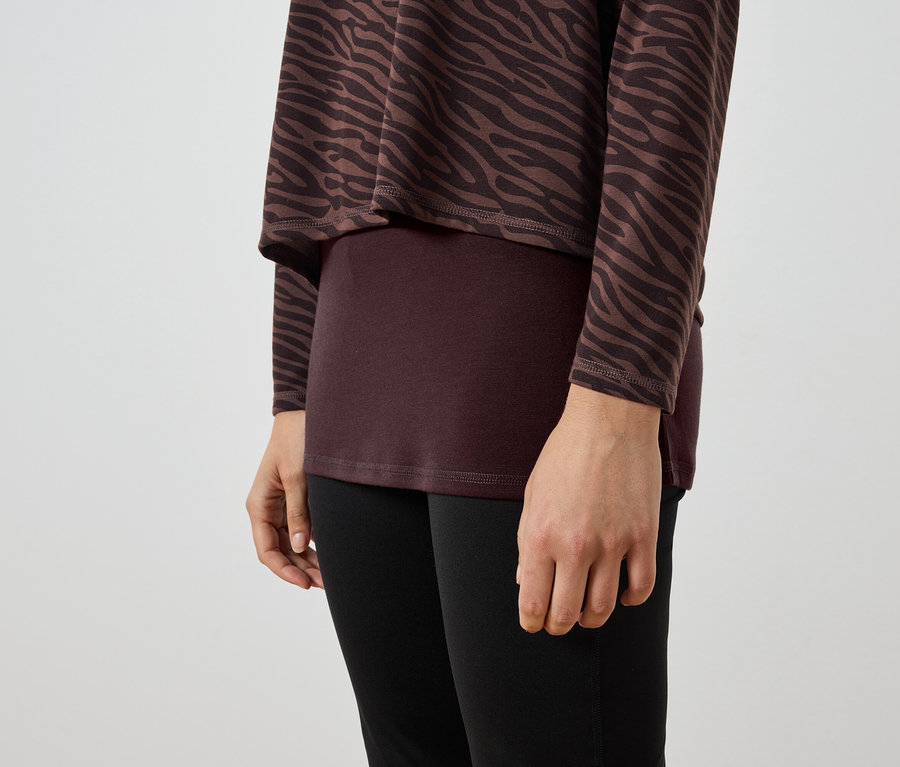 Egy nő részlete, aki barna-fekete zebrás tunikát, bordó felsőt és fekete leggingset visel.