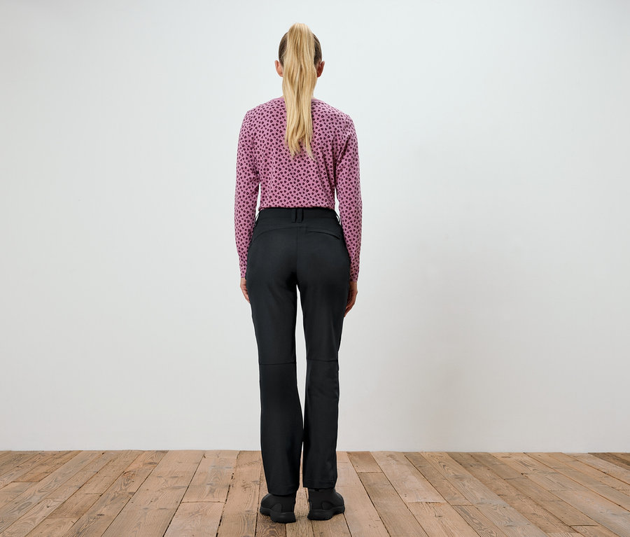 Egy nő áll háttal a kamerának, lila, mintás felsőt és fekete nadrágot visel.