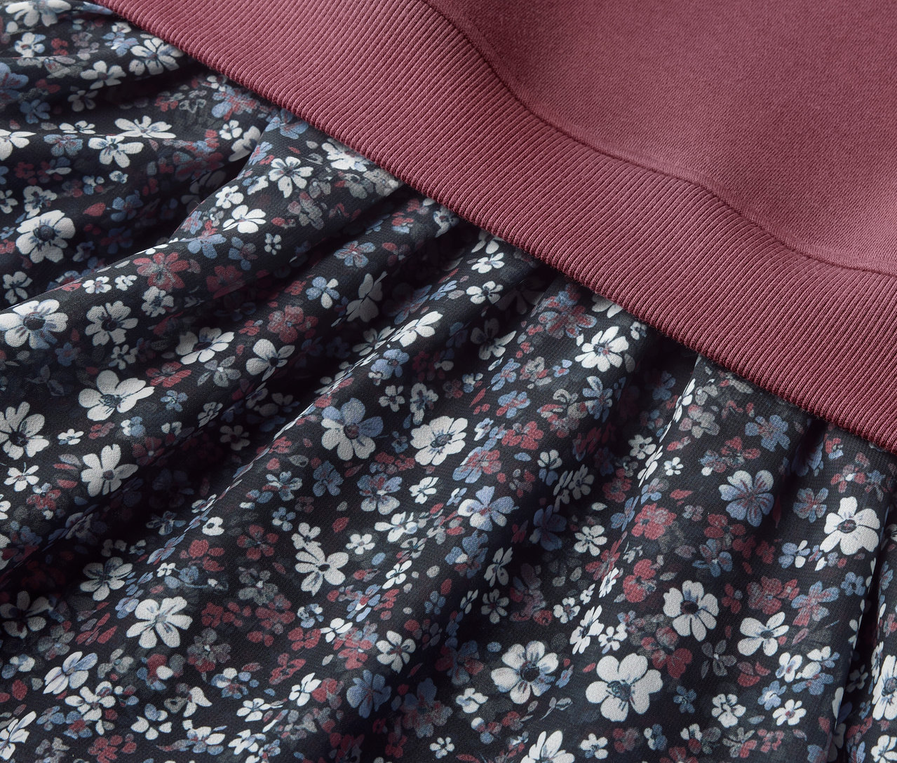 Egy Kinder-Sweatkleid részlete virágmintás szoknyával és bordó felsőrésszel.