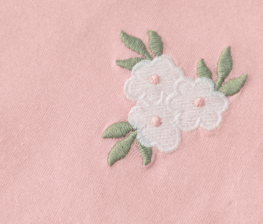 Három hímzett fehér virág zöld levelekkel rózsaszín anyagon közelről.