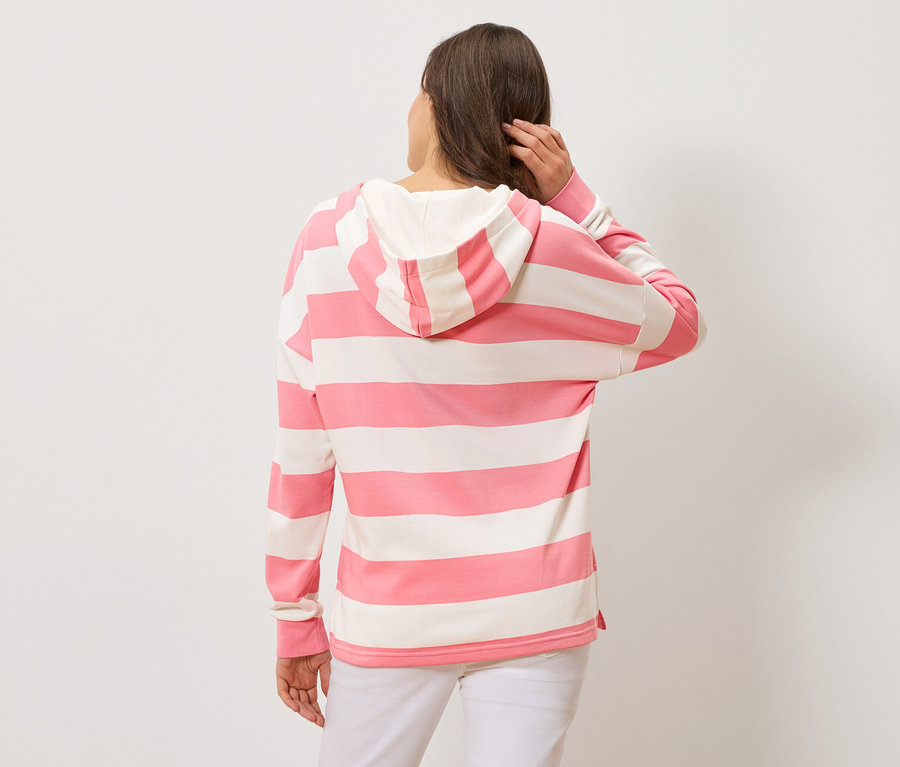 Hátulról látható nő rózsaszín-fehér csíkos kapucnis pulóvert és fehér nadrágot visel.