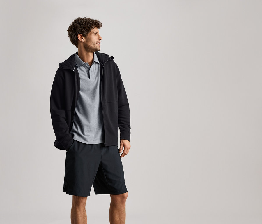 Férfi visel fekete szabadidőfelsőt szürke galléros póló és fekete rövidnadrág fölött.