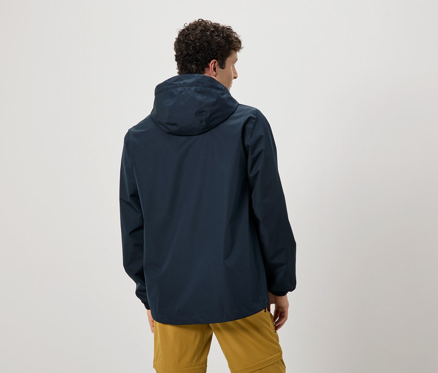 Hátulnézet egy göndör hajú férfiról, aki sötétkék kapucnis esőkabátot és okkersárga nadrágot visel.