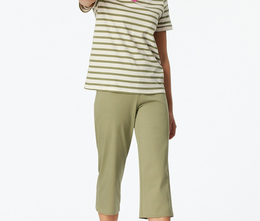 Nő áll mezítláb, csíkos V-nyakú pólót és zöld capri nadrágot visel.