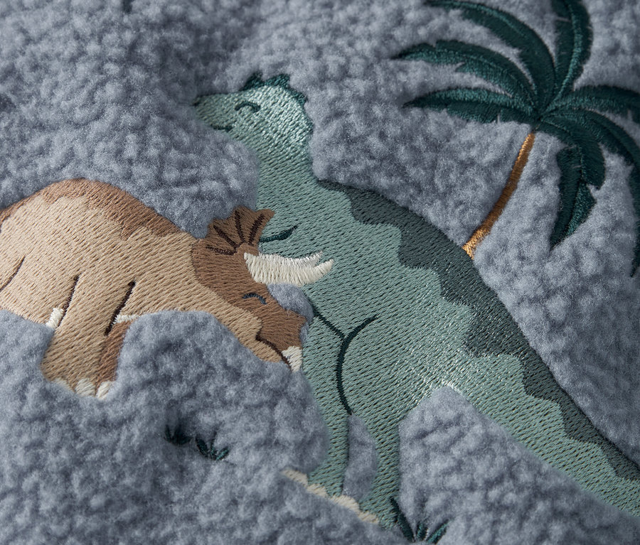 Egy szürke szövet közeli képe hímzett dinoszauruszokkal és egy pálmafával.