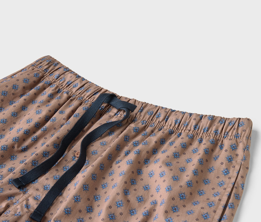 Egy bézs színű nadrág közeli képe kék virágmintával és sötétkék húzózsinórral.