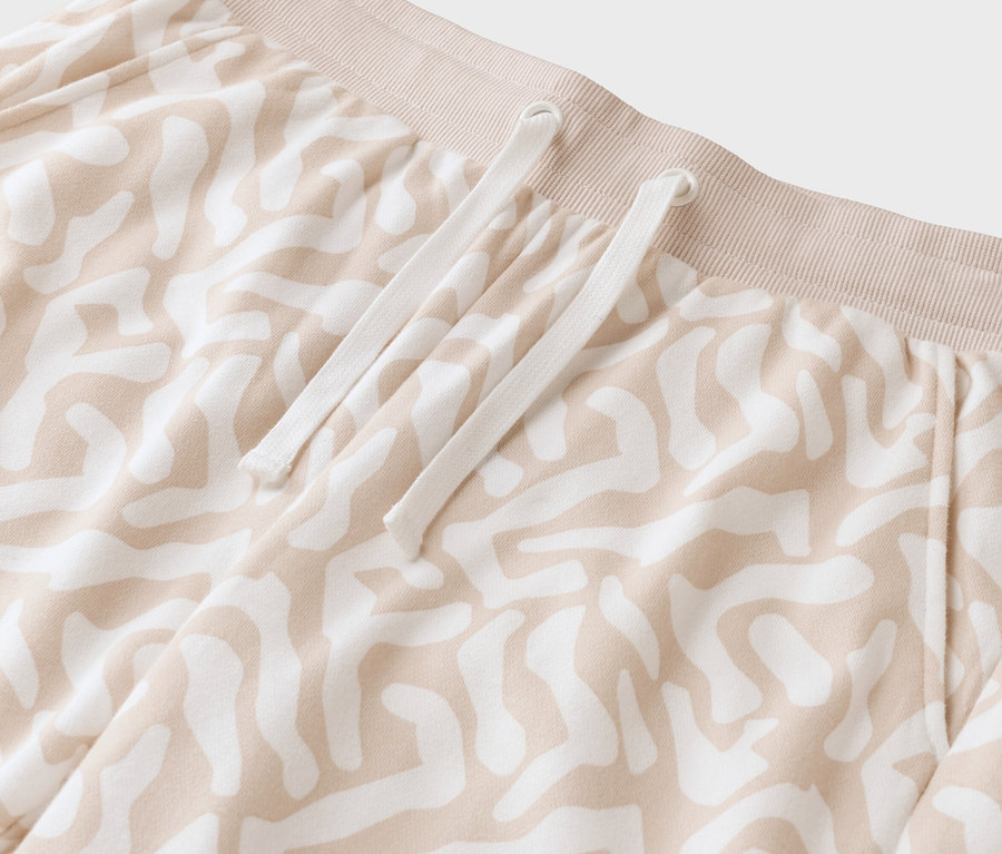 Egy bézs színű, mintás nadrág közeli képe fehér húzózsinórral.