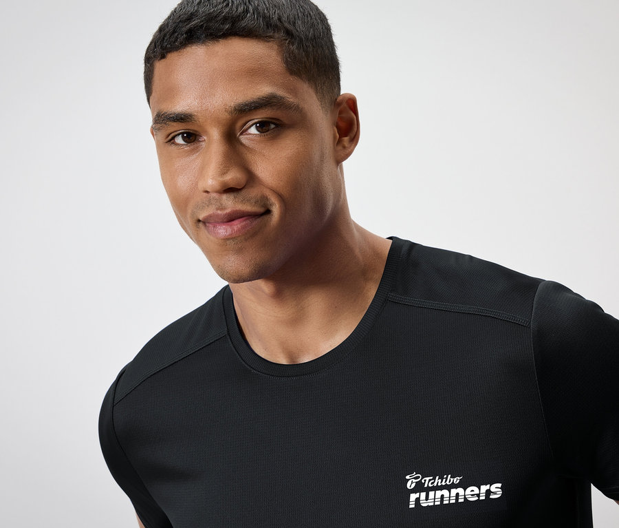 Egy sötét bőrű férfi "Tchibo runners" feliratú fekete pólót visel.