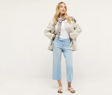 Egy nő áll, és Angels denim »Linn City« bokát szabadon hagyó farmernadrágot, fehér pólót, blézert és sálat visel.