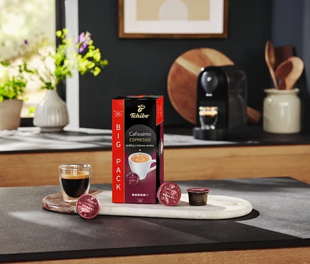 Eszpresszós pohár áll a Cafissimo Espresso csomag és kapszulák mellett egy márványtálcán.