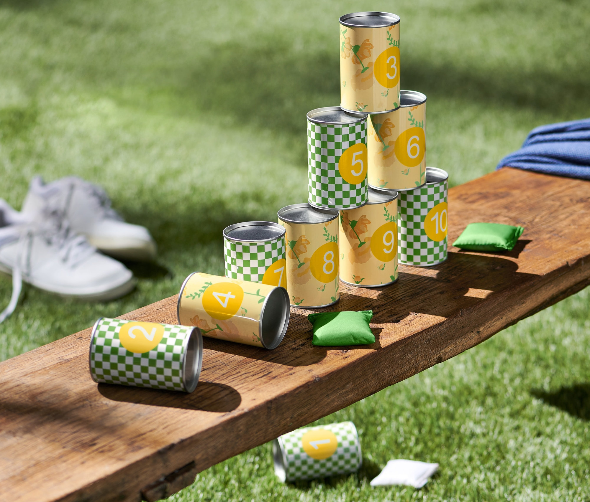 Egy padon egy dobozos célbadobó játék dobozokból álló piramis és dobózsákok láthatók.