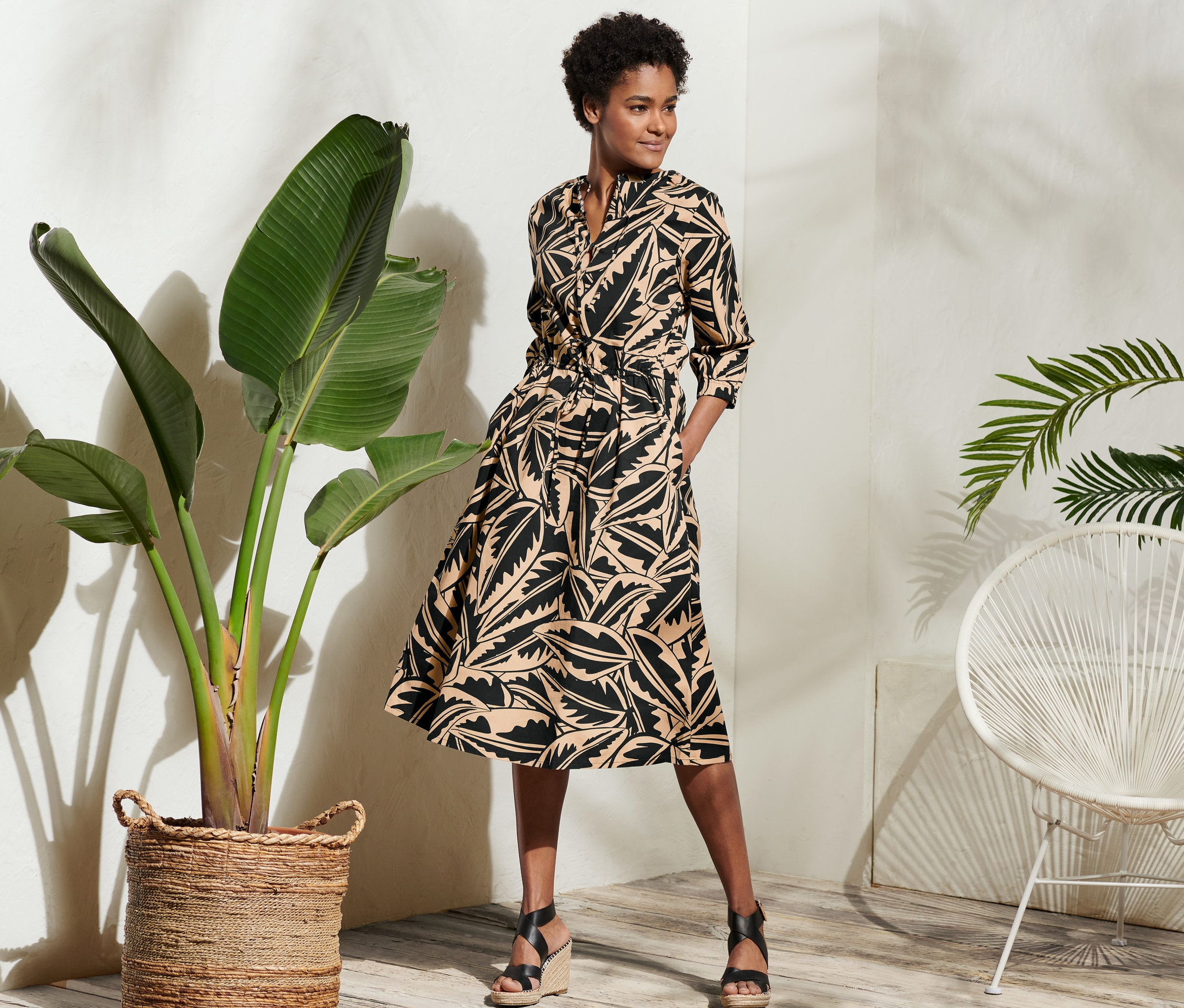 Nő pózol egy pálmalevél mintás poplin ruhában.