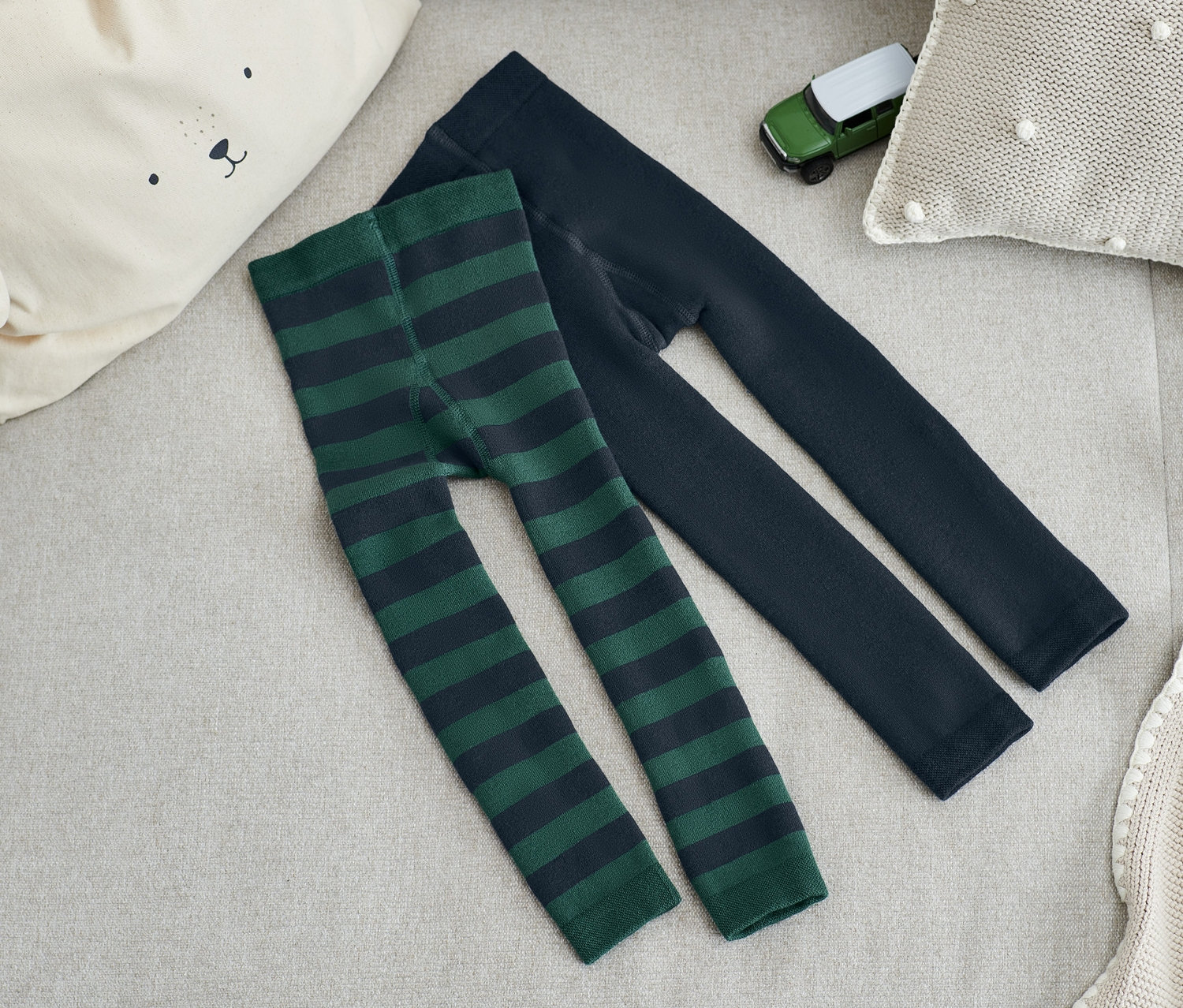 Két pár termoleggings fekszik egy bézs kanapén, egyik zöld csíkos, a másik sötétkék.