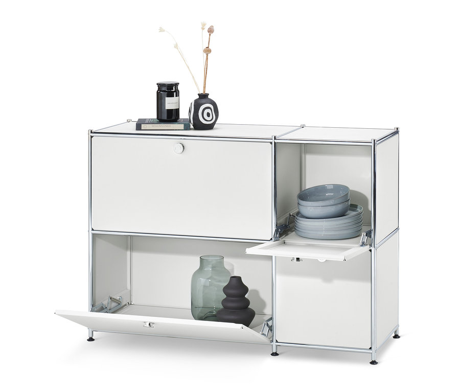 Fehér »CN3« komód 4 lenyitható ajtóval. A komód tetején váza és gyertya, a komódban tányérok és tálak találhatók.