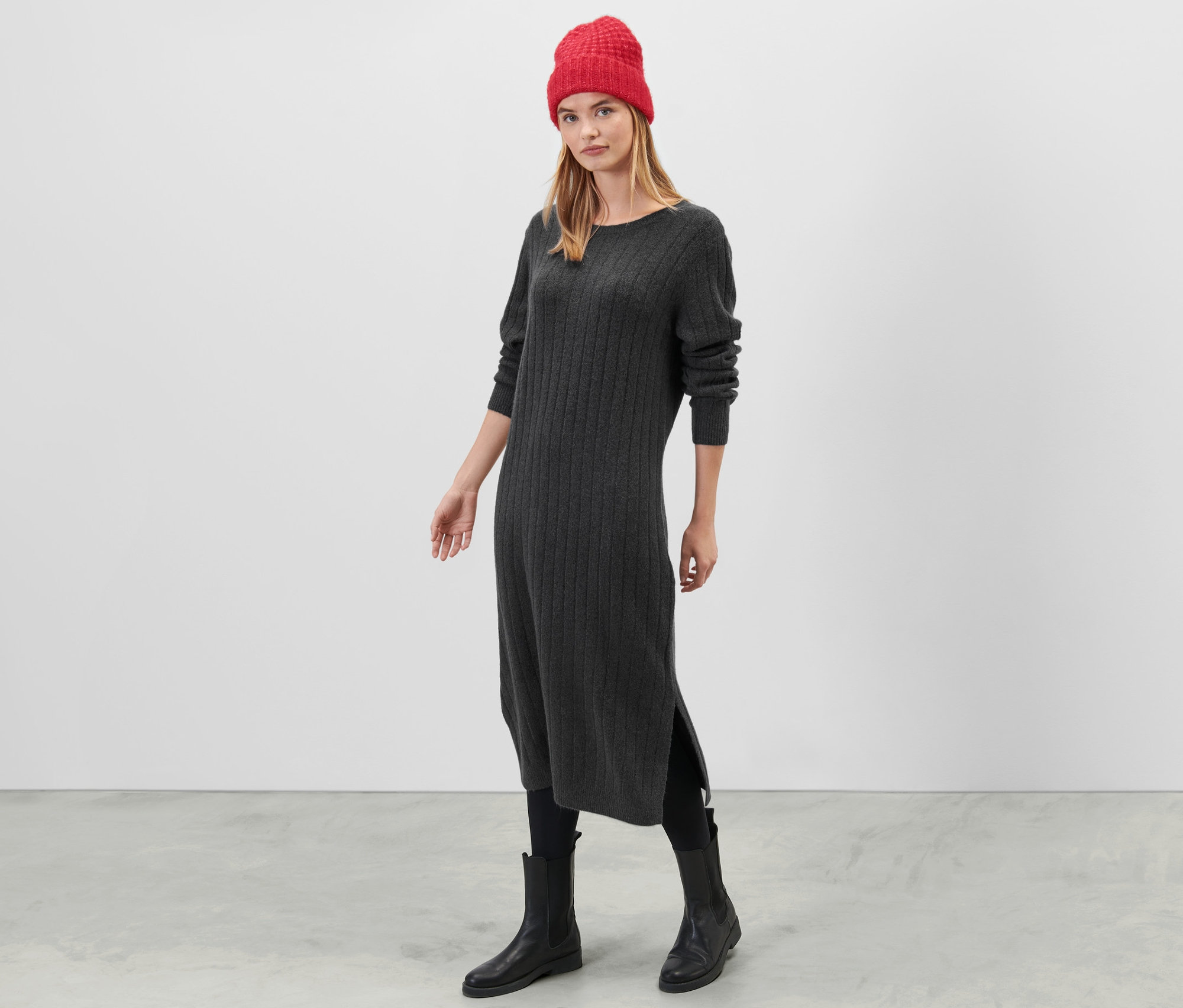 Egy nő áll szürke, bordás kötésű ruhában.