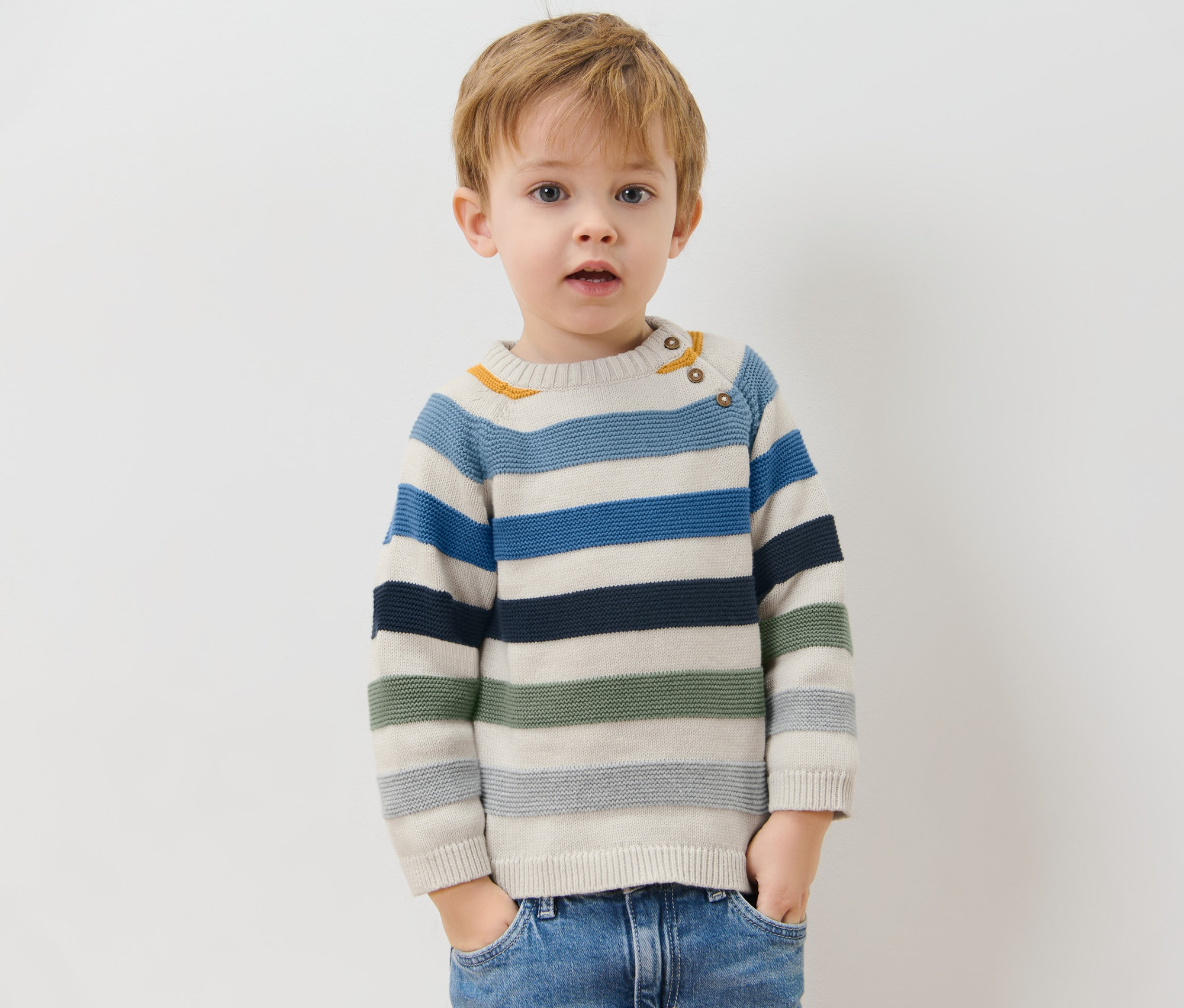 Egy fiú csíkos kötött pulóverben pózol.