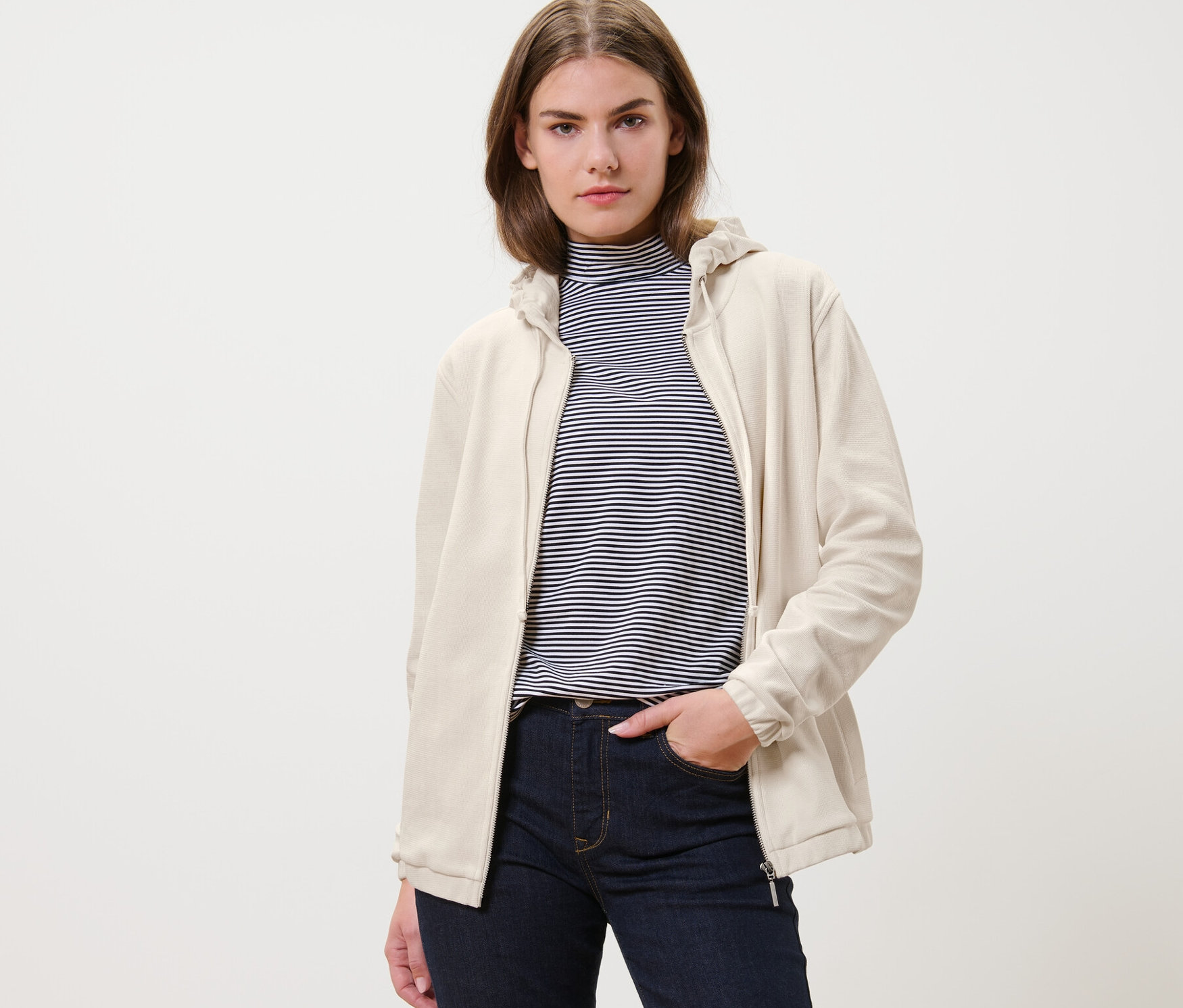 Nő krémfehér szabadidőfelsőt és farmert visel.