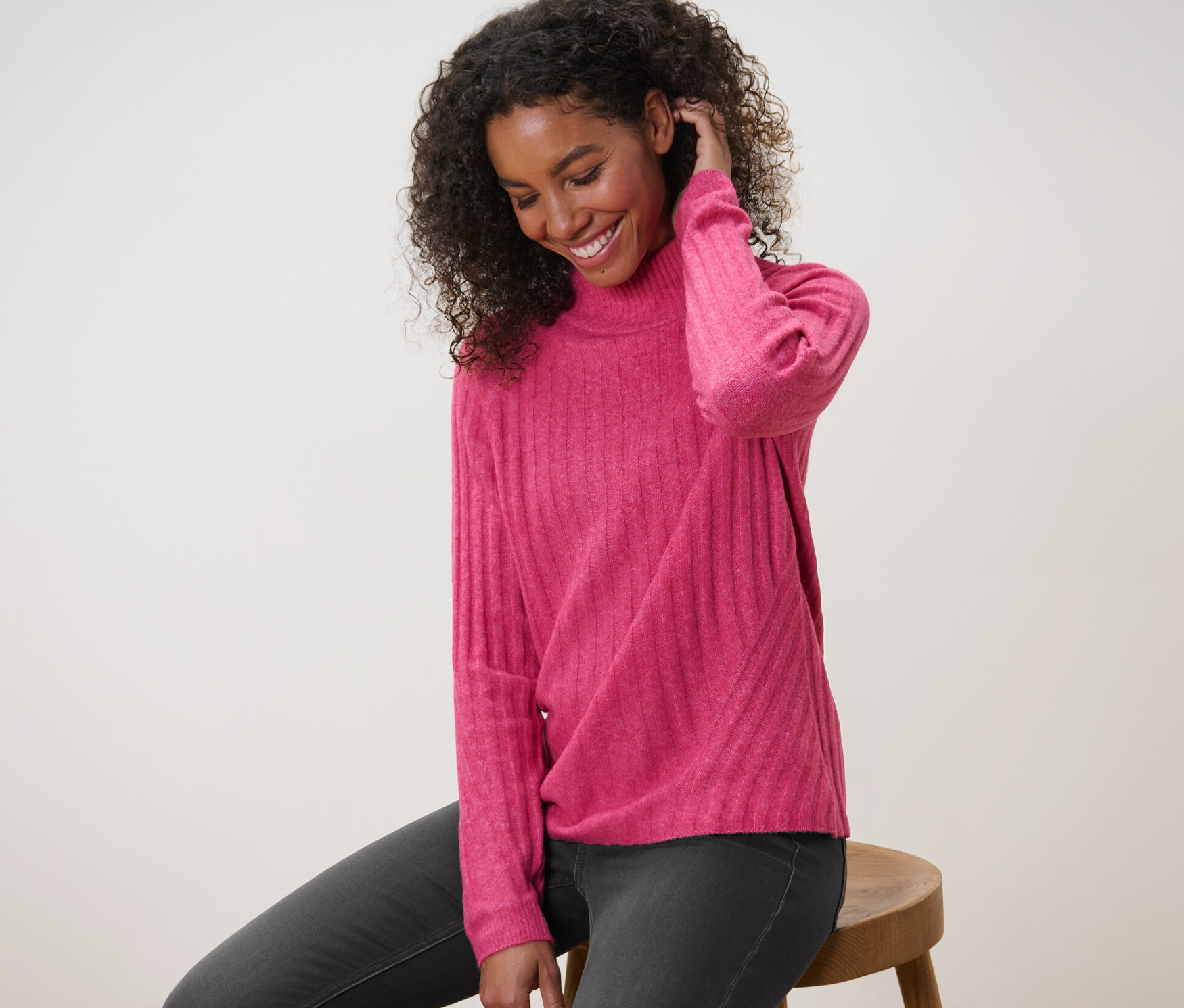 Nő ül egy széken, málna piros kötött pulóvert visel.