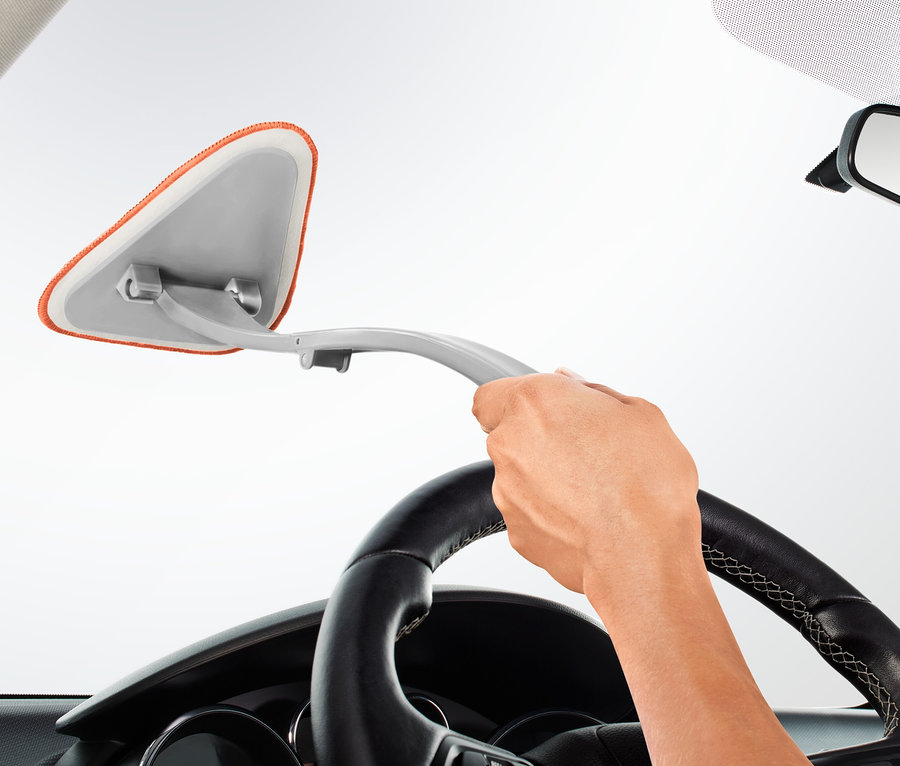 Egy kéz autós szélvédőtisztítót tart és tisztítja az autó szélvédőjét.