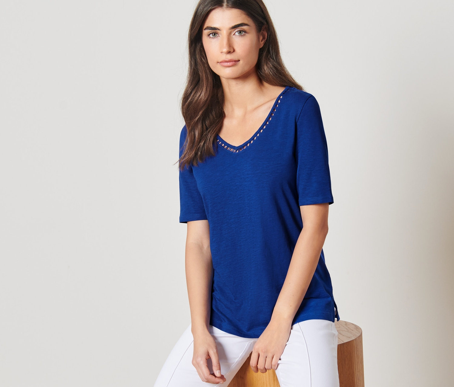 Egy nő ül egy széken, kobaltkék felsőt és fehér nadrágot visel.