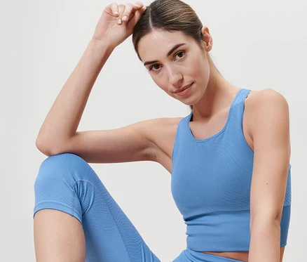 Egy nő ül, és kék, seamless sport crop topot és leggingst visel.