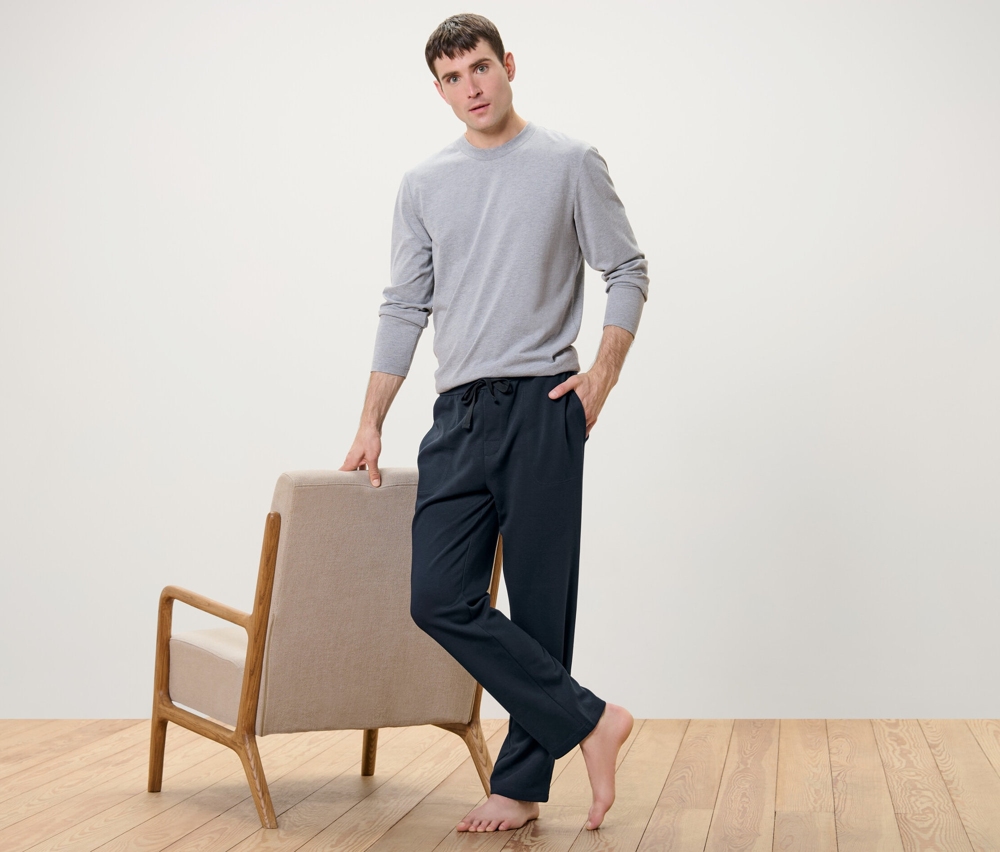 Egy férfi egy fotel mellett pózol, sötétkék férfi szabadidőnadrágot és szürke pólót visel.