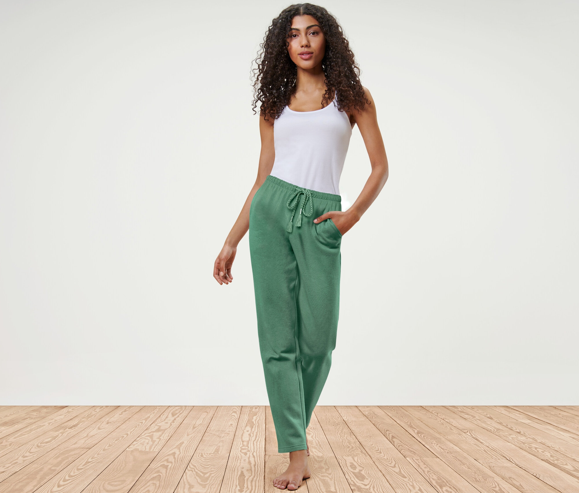 Nő pózol zöld női szabadidőnadrágban és fehér felsőben.