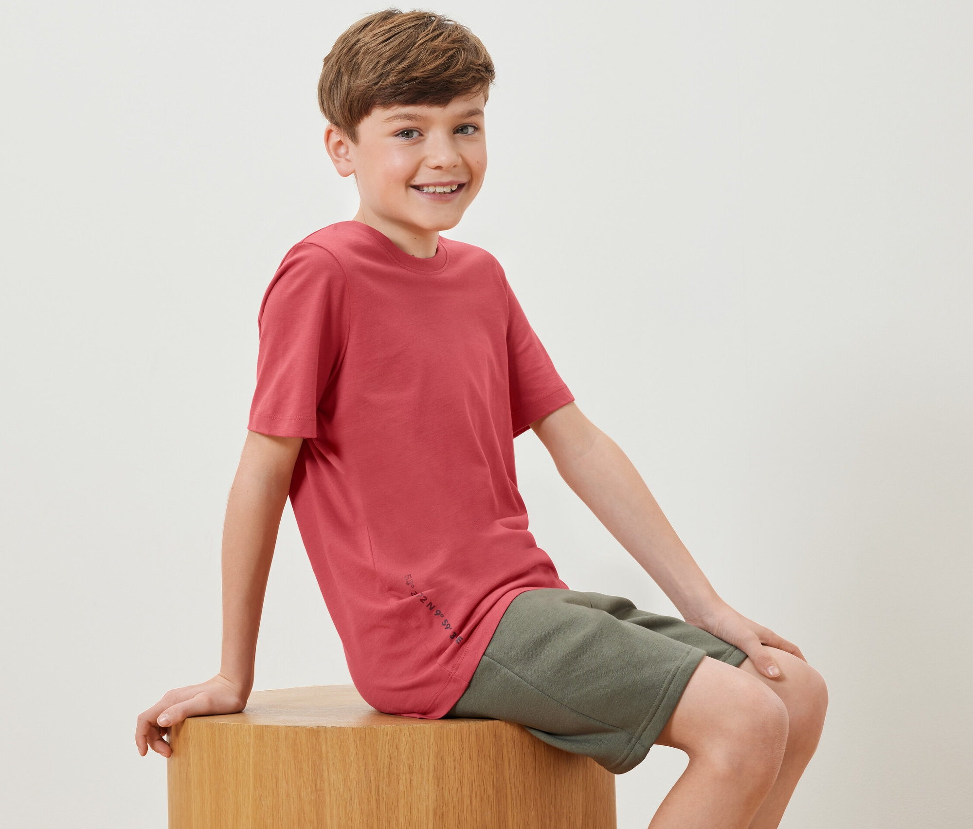 Egy fiú ül egy fakockán, és egy piros pólót visel a 2 gyerek póló szettből.