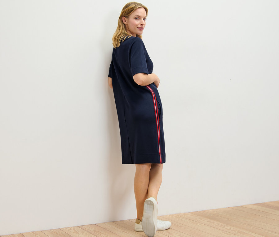 Nő néz a válla fölött és pózol egy sötétkék, csíkos, női lezser ruhában.