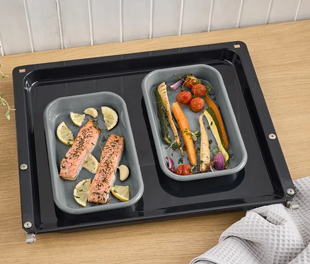 Két szürke zománcos grilltálca lazaccal, citrommal és zöldségekkel egy sütőlemezen.