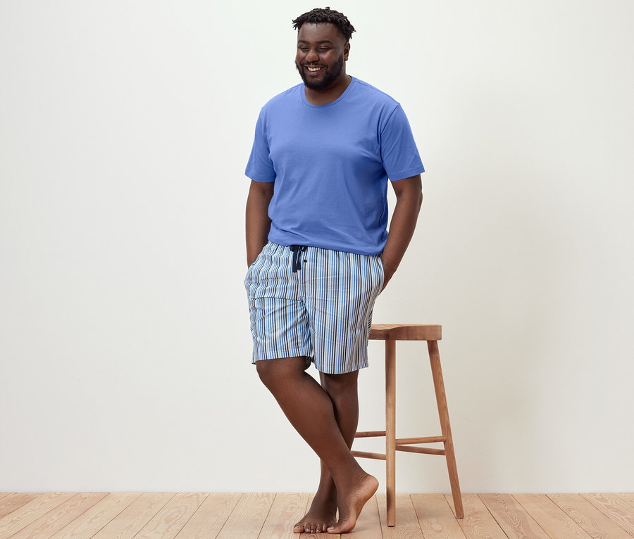 Férfi támaszkodik a székre, csíkos rövidnadrágos pizsamában.