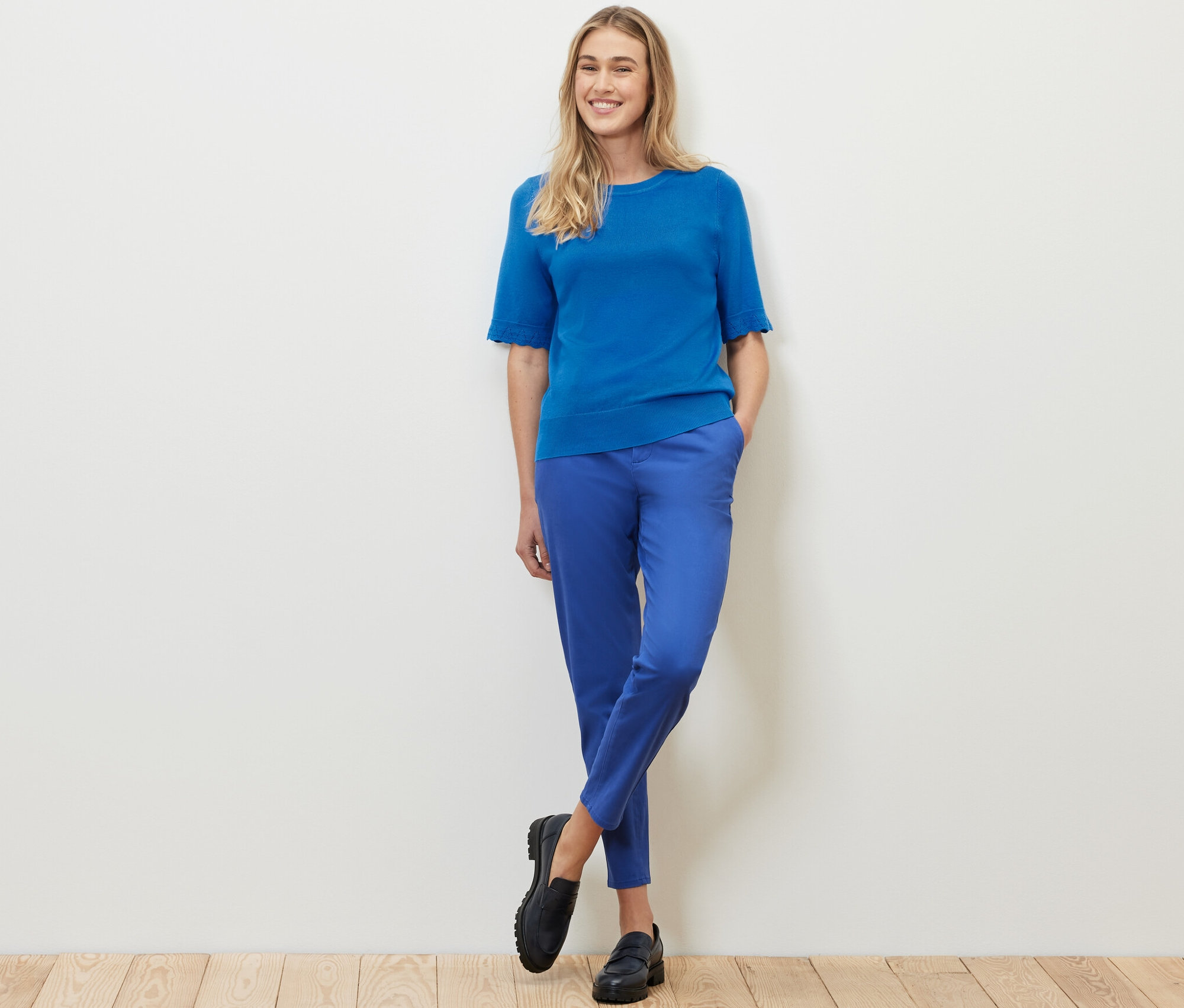Nő áll kobaltkék, finom kötésű pulóverben és kék nadrágban.