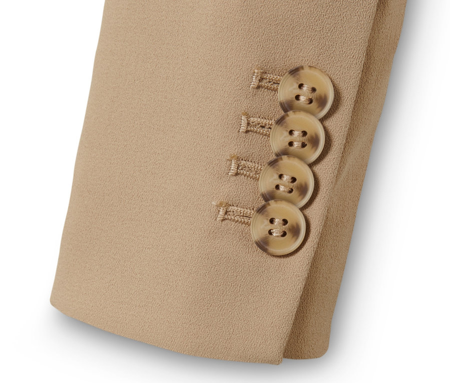 Egy bézs színű, szőtt blézer részlete barna gombokkal az ujján.