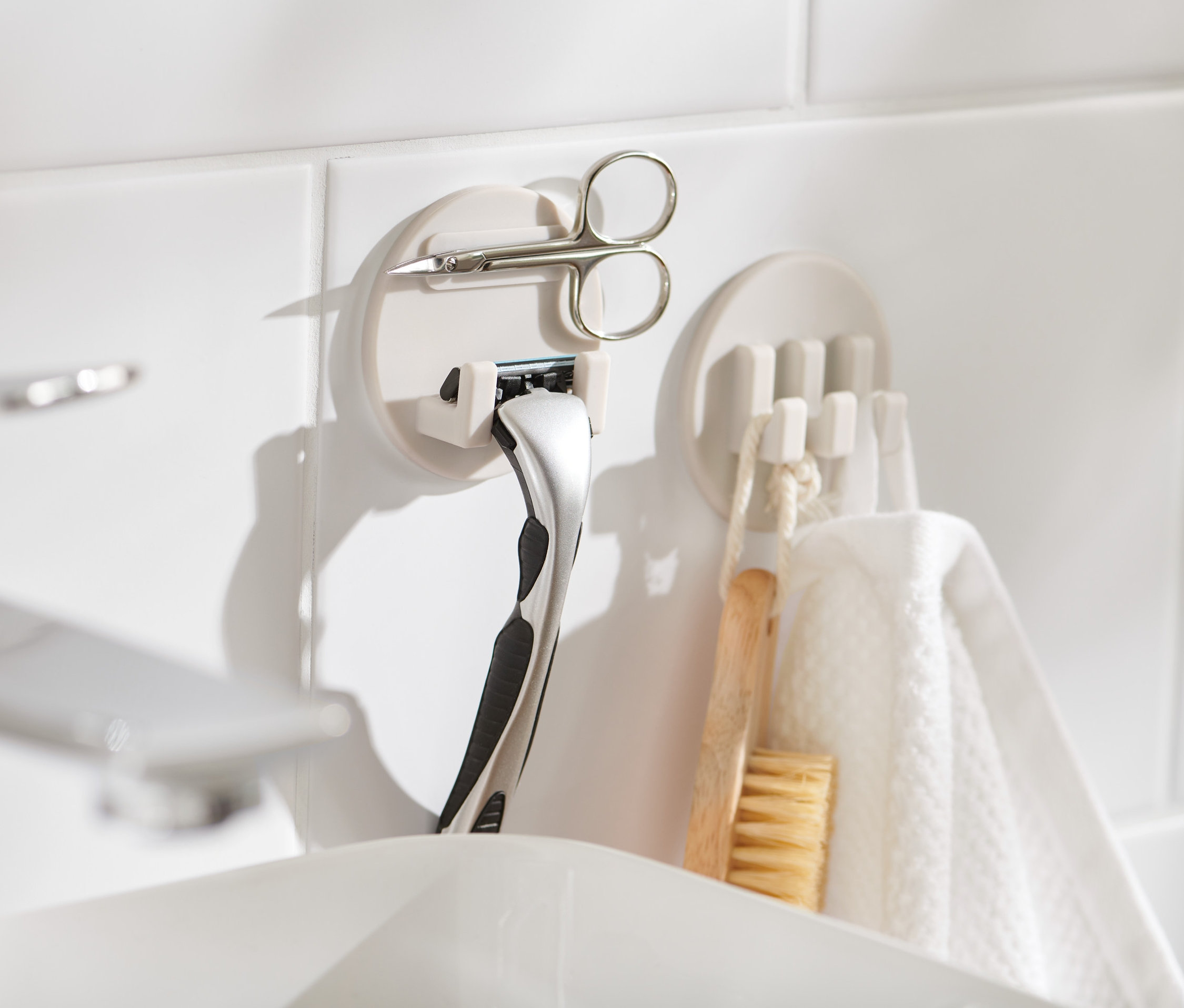 Két öntapadós akasztó szett fehér csempén, az egyiken borotva és olló.