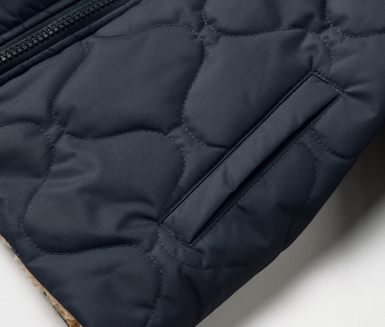 Részlet egy steppelt, kifordítható Kinder-Wendejacke zsebével és cipzárjával.