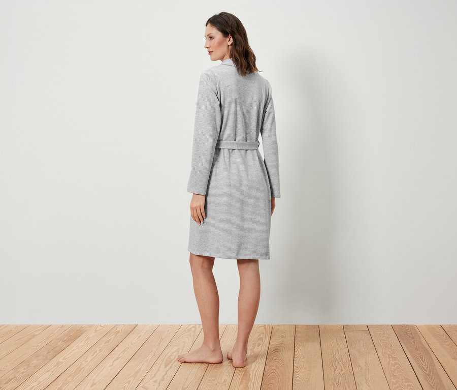 Egy nő áll háttal, szürke köntöst visel.