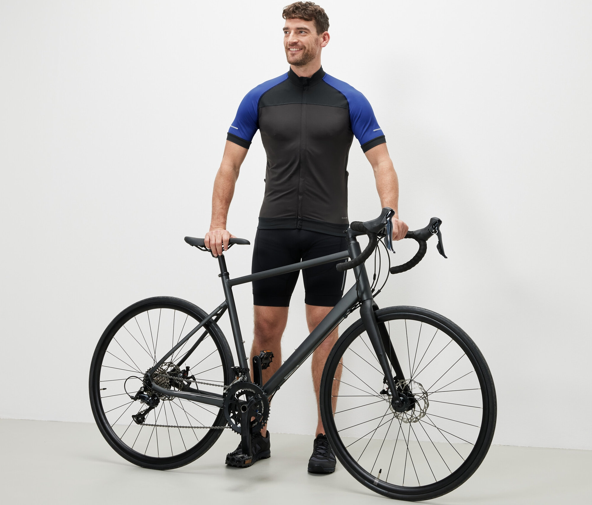 Férfi áll egy kerékpár mellett, kék kerékpáros trikóban.