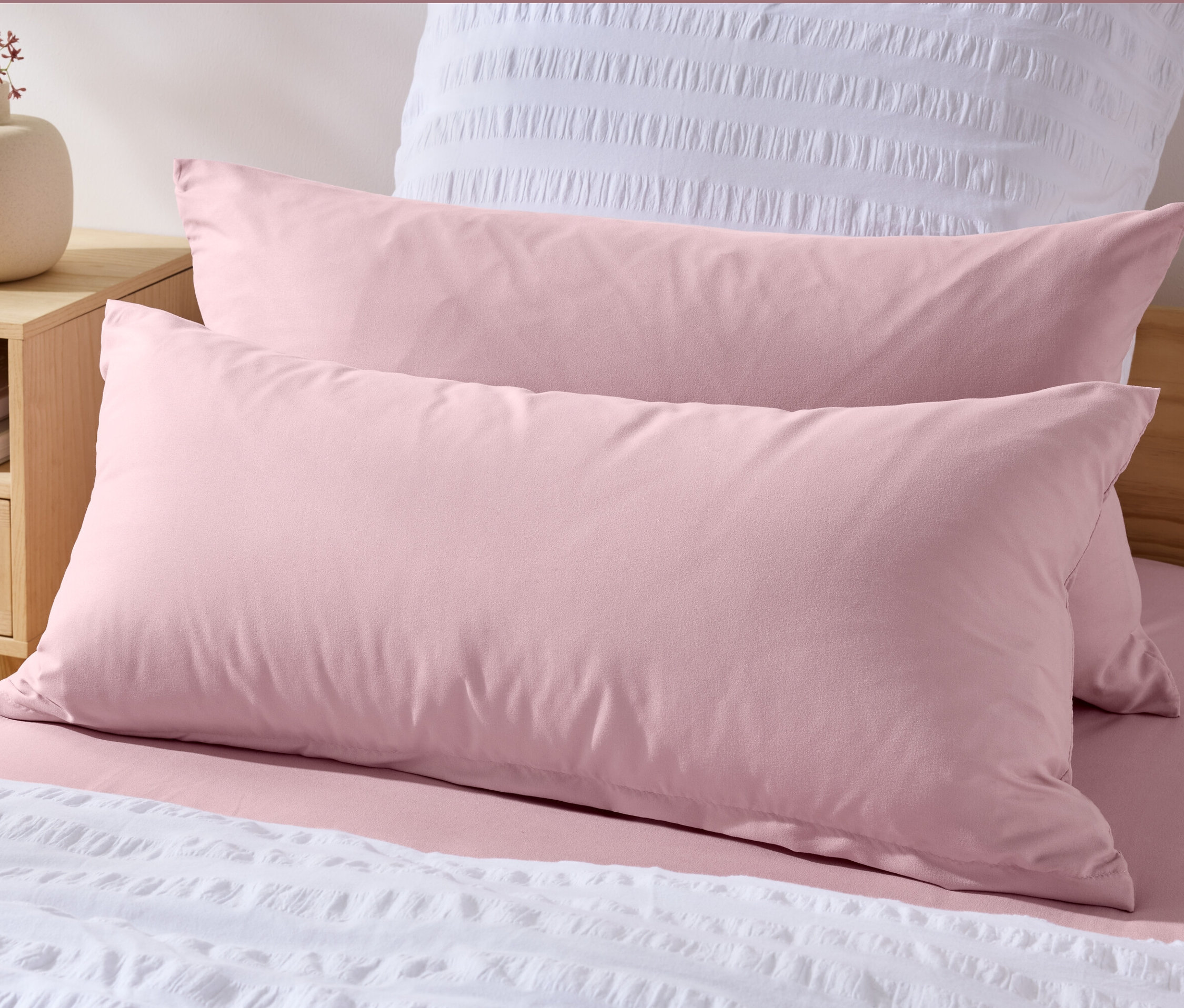 Két rózsaszín mikroszálas párnahuzat (kb. 80 x 40 cm) egy ágyon, fehér ágytakaróval.