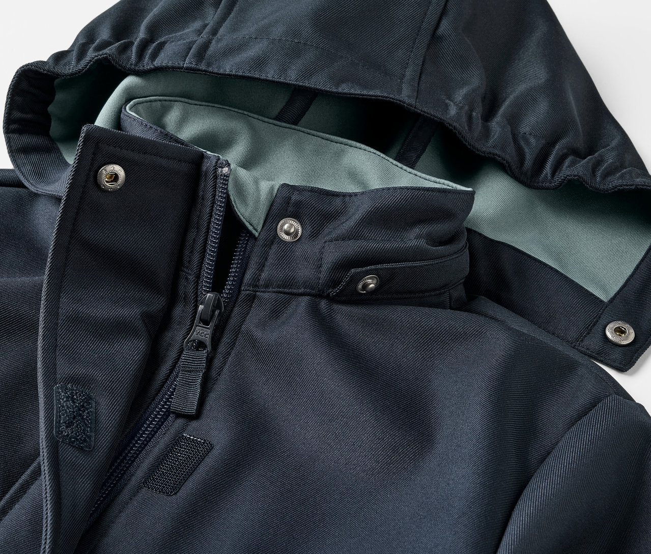 Egy gyermek softshell kabát részlete, kapucnival és cipzárral.