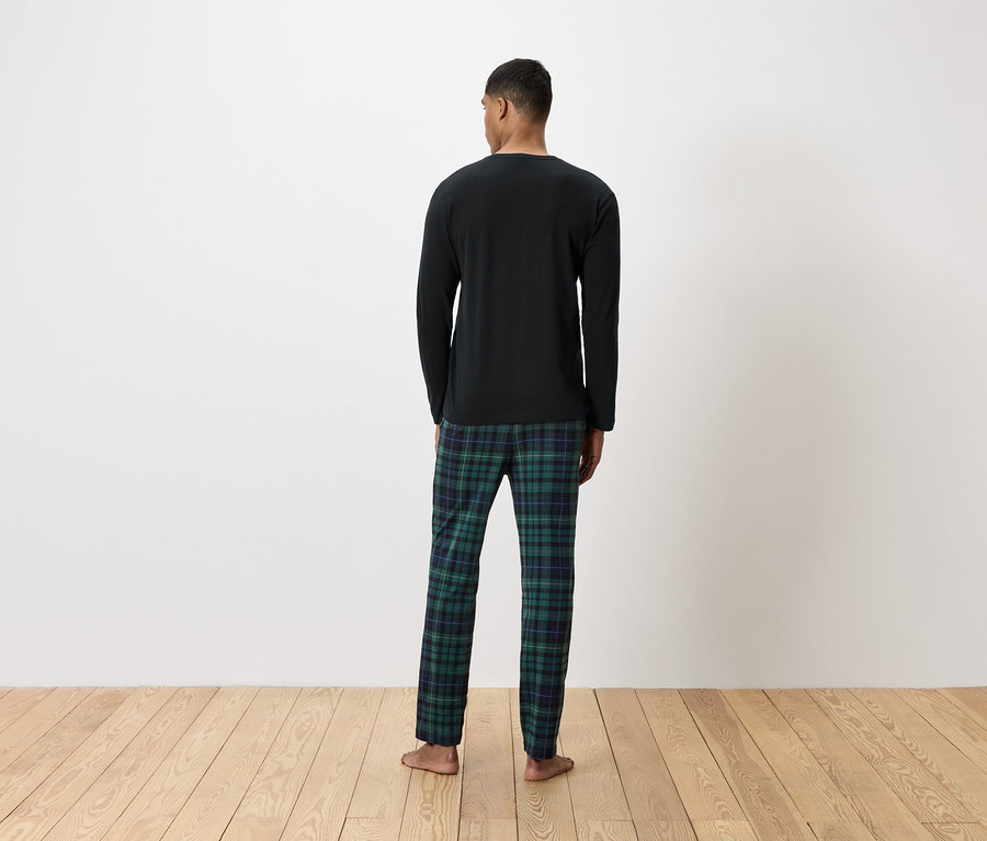 Egy férfi hátulról egy fekete, hosszú ujjú inget és egy zöld kockás pizsama nadrágot visel.