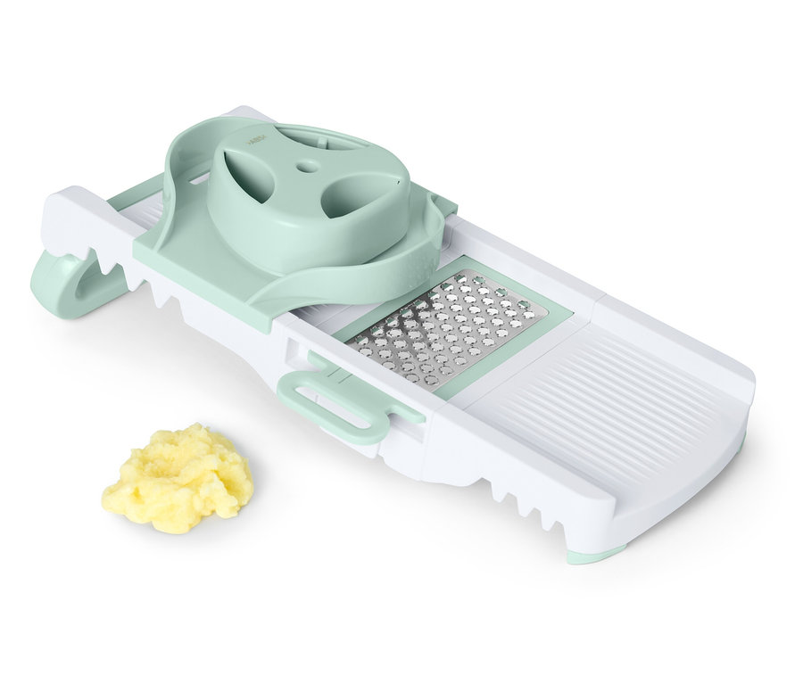 Egy fehér és zöld mandolin szeletelő egy halom vágott zöldséggel.