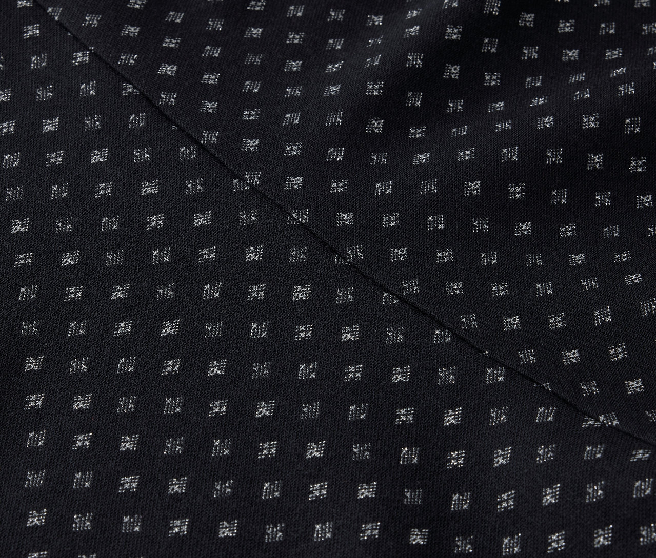 Egy fekete szövet részlete, szabályos mintával, apró fehér négyzetekkel és egy átlós varrással.