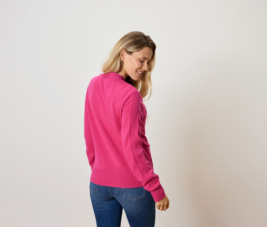 Nő néz lefelé, rózsaszín pulóvert és farmert visel.