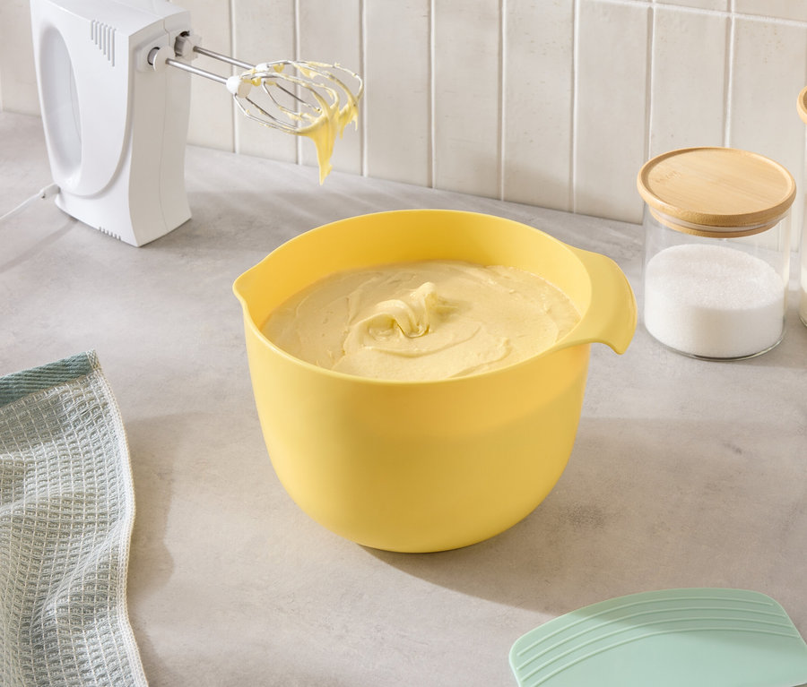 A konyhapulton egy sárga tál tésztával, egy mixer, valamint cukorral és liszttel teli üvegek állnak.