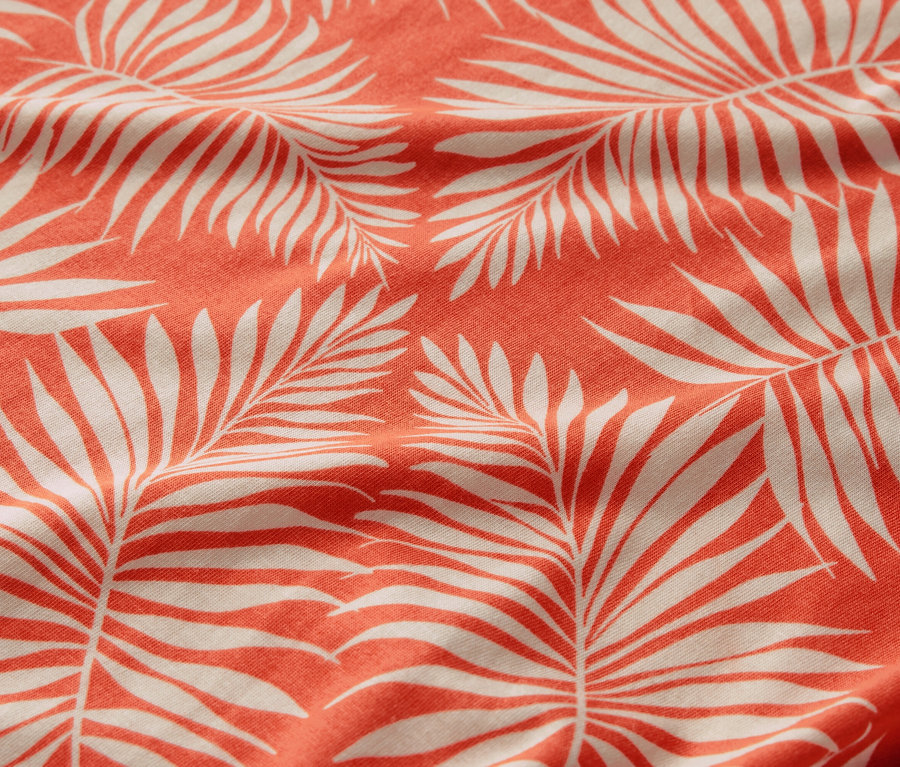 Egy nyomott mintás női pólóblúz közeli képe, fehér pálmalevél mintával, korall háttéren.