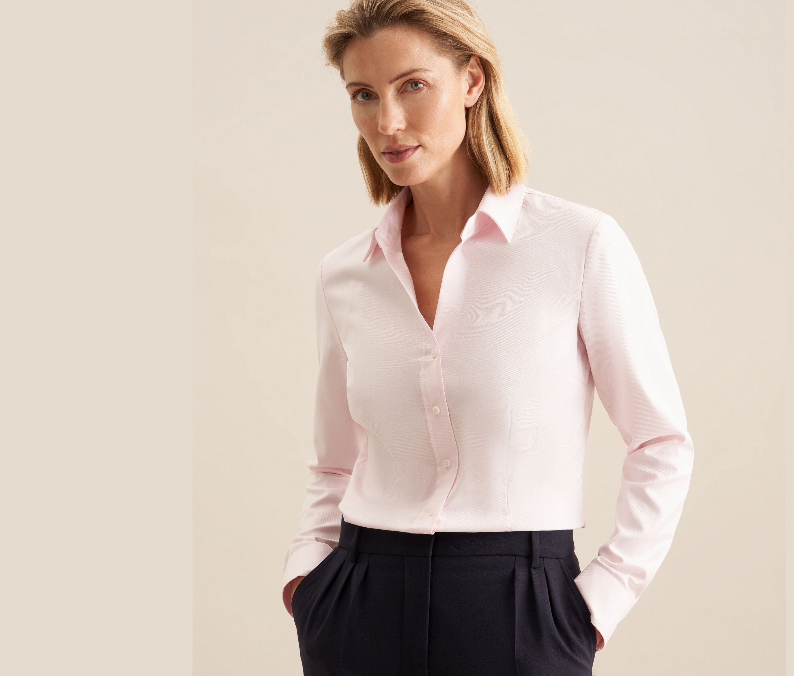 Nő visel egy rózsaszínű Seidensticker twill blúzt és egy sötétkék nadrágot.