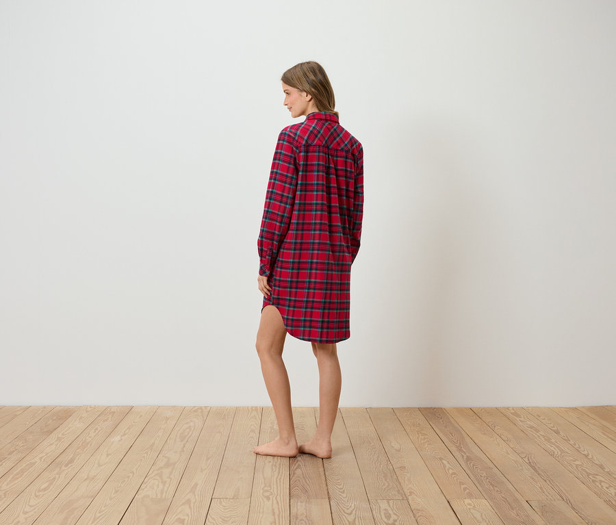 Egy nő oldalra állva piros kockás flanel ingruhát visel.